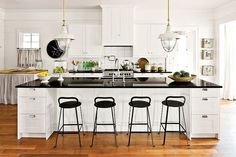 a large kitchen with white cabinets and black counter tops, along with four stools