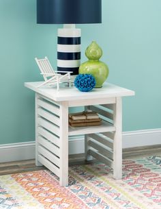 a white table topped with a green vase next to a blue and white striped lamp