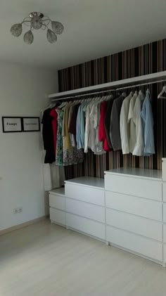 an organized closet with clothes hanging on the wall and drawers in front of it, next to a chandelier