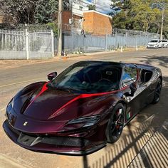 a red and black sports car parked on the side of the road next to a fence