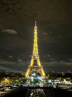 the eiffel tower lit up at night with cars passing by in front of it