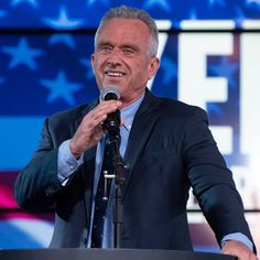 a man standing at a podium with a microphone in his hand and an american flag behind him