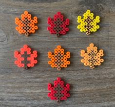 six perler beads arranged in the shape of flowers on a wooden surface, each with different colors