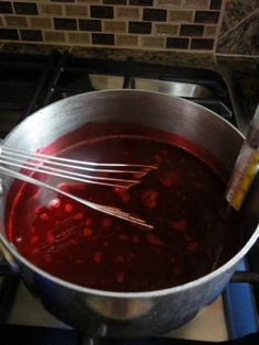 a pot filled with red liquid and whisk on top of a stovetop