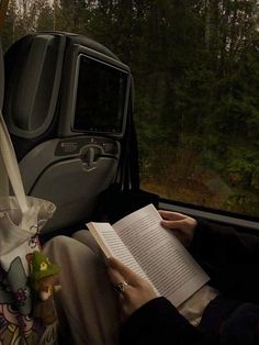 a person sitting in the back seat of a vehicle reading a book while holding an umbrella