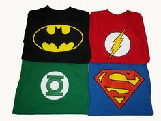 four t - shirts with batman, superman and green lantern logos on them are laying on a bed