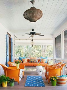 an outdoor living area with orange chairs, blue rug and potted plants on the porch