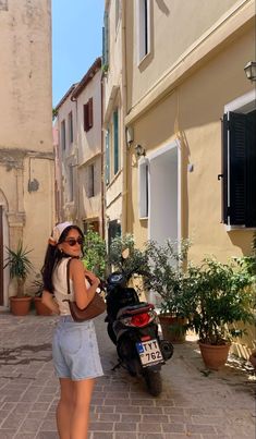 a woman standing next to a motor scooter on a brick road in front of buildings