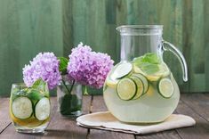 a pitcher of water with cucumbers and lemon slices in it next to some flowers