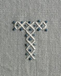 a cross stitched into the side of a piece of fabric with blue beads on it