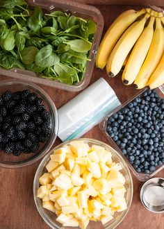 various fruits and vegetables are arranged in bowls on a table with banana's, blueberries, spinach