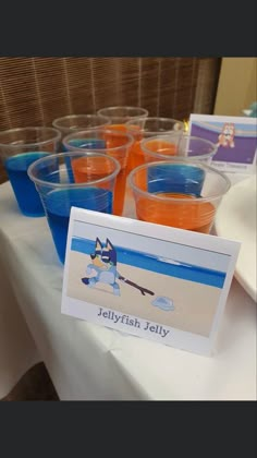 plastic cups filled with orange and blue liquid sitting on top of a white tablecloth