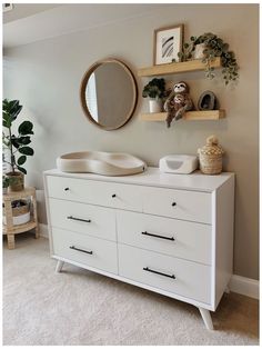 a white dresser sitting next to a mirror and potted plant