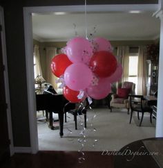 red and pink balloons hanging from the ceiling in a living room with piano behind them