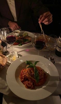 a man is eating spaghetti at a table with wine glasses and bread on the side