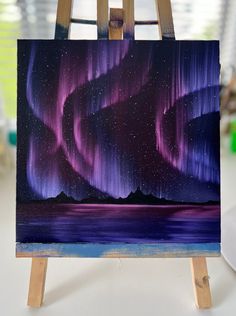 an easel with a painting on it that has the aurora lights painted on it