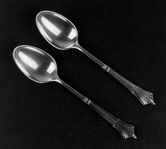 two silver spoons sitting next to each other on a black surface