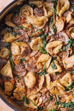 pasta with mushrooms and spinach in a skillet on a wooden counter top, ready to be eaten