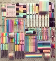 many different colored pens and pencils are arranged on a lace tablecloth with a calculator