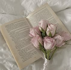 a bouquet of pink flowers sitting next to an open book on top of a bed