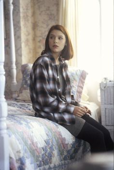 a woman sitting on top of a bed next to a window