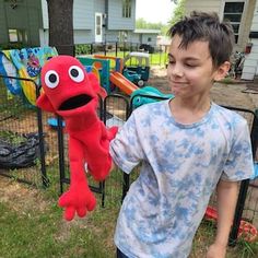 a young boy standing next to a red stuffed animal in front of a play yard