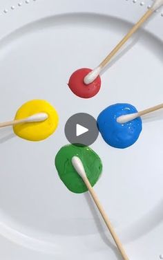 four colorful marshmallows on a white plate with toothpicks