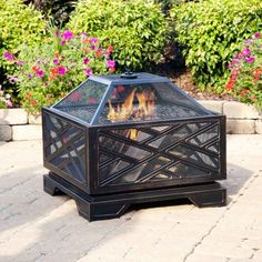 an outdoor fire pit sitting on top of a brick patio next to flowers and bushes