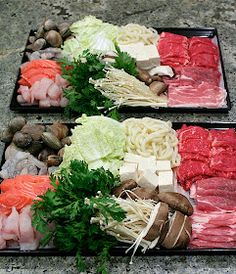 two trays filled with meat and vegetables on top of a stone floor next to each other