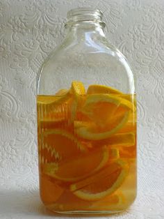 a glass bottle filled with orange slices on top of a white tableclothed surface