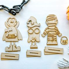 three wooden cutouts of halloween characters on a white table with silverware and pumpkins