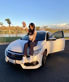 a woman sitting on the hood of a white car in front of a body of water