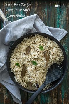 a pan filled with rice and vegetables on top of a wooden table next to a fork