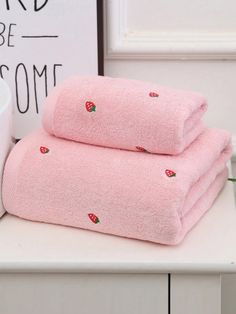 two pink towels sitting on top of a white counter next to a cup and sign