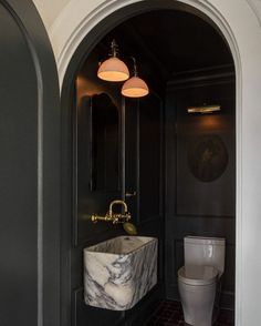 a white toilet sitting next to a bathroom sink under a light over a marble sink