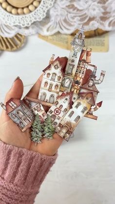 a hand holding a miniature model of a house with trees on it's roof