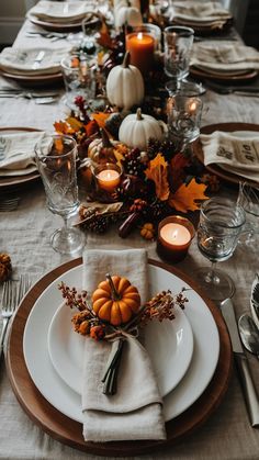 a table set for thanksgiving dinner with white plates and silverware, candles and pumpkins