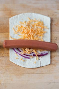 a hot dog bun with cheese and onions on it sitting on a cutting board next to a knife