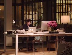 a woman sitting at a desk with a laptop computer in front of her and flowers on the table