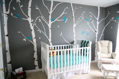 a baby's room decorated in grey and white with trees painted on the wall