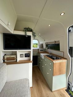 the interior of an rv with wood flooring and green cabinets, television on wall