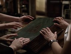 several hands reaching for an old book on a table with other people's hands