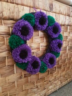 a purple and green knitted wreath sitting on top of a wicker basket next to a wall