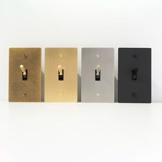 four different types of light switch plates on a white surface with one black, one gold and one silver