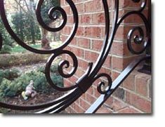 an iron gate on the side of a brick building with a garden in the background