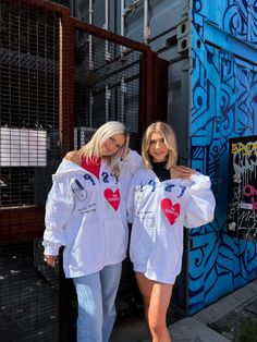 two beautiful women standing next to each other in front of a blue and white wall