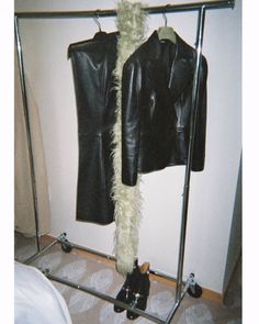 a black leather jacket hanging on a clothes rack next to a white wall and carpeted floor