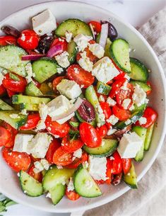 a white bowl filled with cucumbers, tomatoes and feta cheese on top of a table