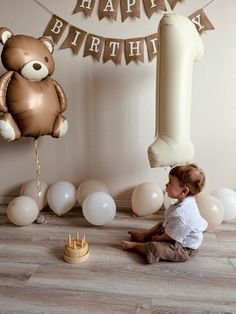 a baby sitting on the floor in front of balloons