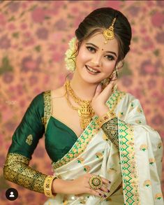 a woman in a green and white sari with gold jewelry on her neck, smiling at the camera